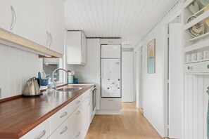 A modern kitchen with white cabinetry, a wooden countertop, and a stainless steel kettle.