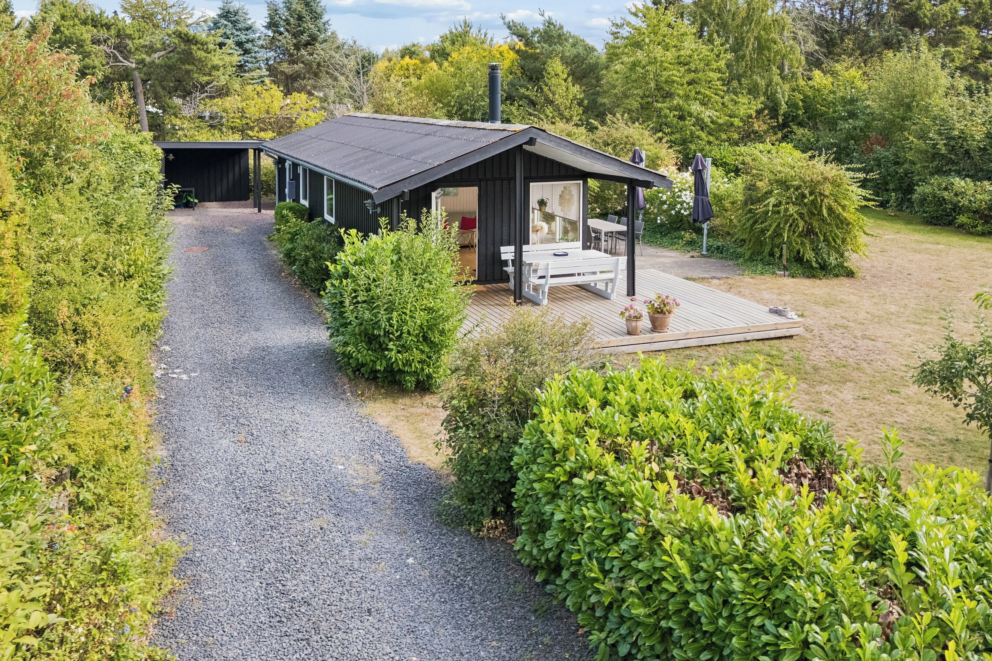 Eine moderne Hütte mit einem Schotterweg, der zu einer Holzterrasse und einer überdachten Sitzgruppe im Freien führt.