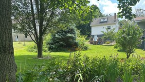 A residential property with a well-maintained lawn, a small deck, and a variety of flowering plants. - Spotless, Quiet 2BR Cottage: Private Deck, Big TV, Yard—Near Museums & Parks (New Brighton)