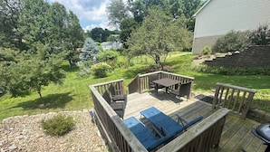 A wooden deck with a table and chairs, surrounded by a garden and trees. - Spotless, Quiet 2BR Cottage: Private Deck, Big TV, Yard—Near Museums & Parks (New Brighton)