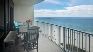 A balcony with a table and chairs, a vase with flowers, and a view of the sea and a pier. - Phoenix Gulf Shores II 1002 (Gulf Shores)