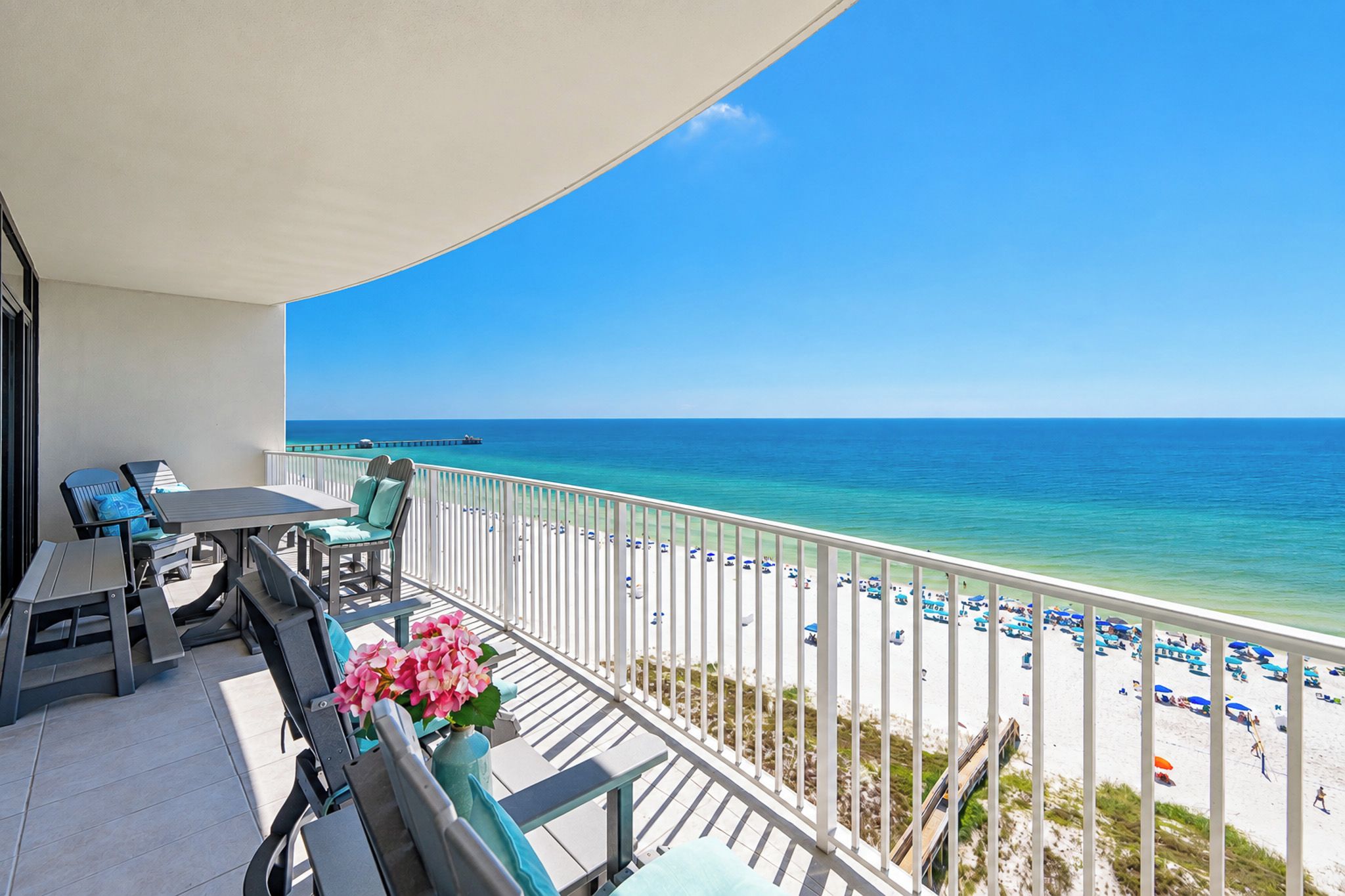 A balcony with a view of the beach, outdoor furniture, and a clear sky.