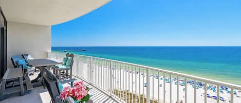 A balcony with a view of the beach, outdoor furniture, and a clear sky.
