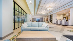 A modern lobby with a light blue sofa, a wooden coffee table, and a reception desk. - Phoenix Gulf Shores II 1002 (Gulf Shores)
