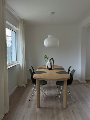 Un comedor con una mesa redonda, sillas negras, una lámpara colgante blanca y un florero con plantas verdes.