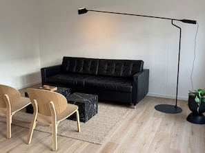 Una sala de estar moderna con un sofá de cuero negro, sillas de madera, una mesa de centro de mármol, una lámpara de pie y una planta en maceta.