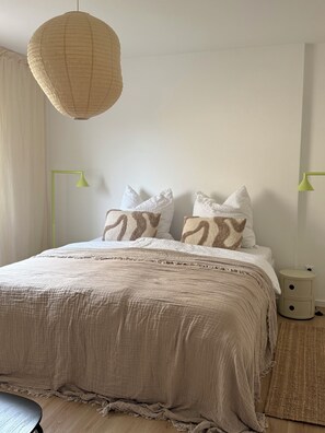Quarto com cama, duas luminárias de cabeceira, um lustre e uma mesinha de cabeceira.