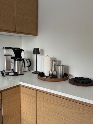 Uma cozinha com cafeteira, chaleira e um tabuleiro com chávenas e um prato.