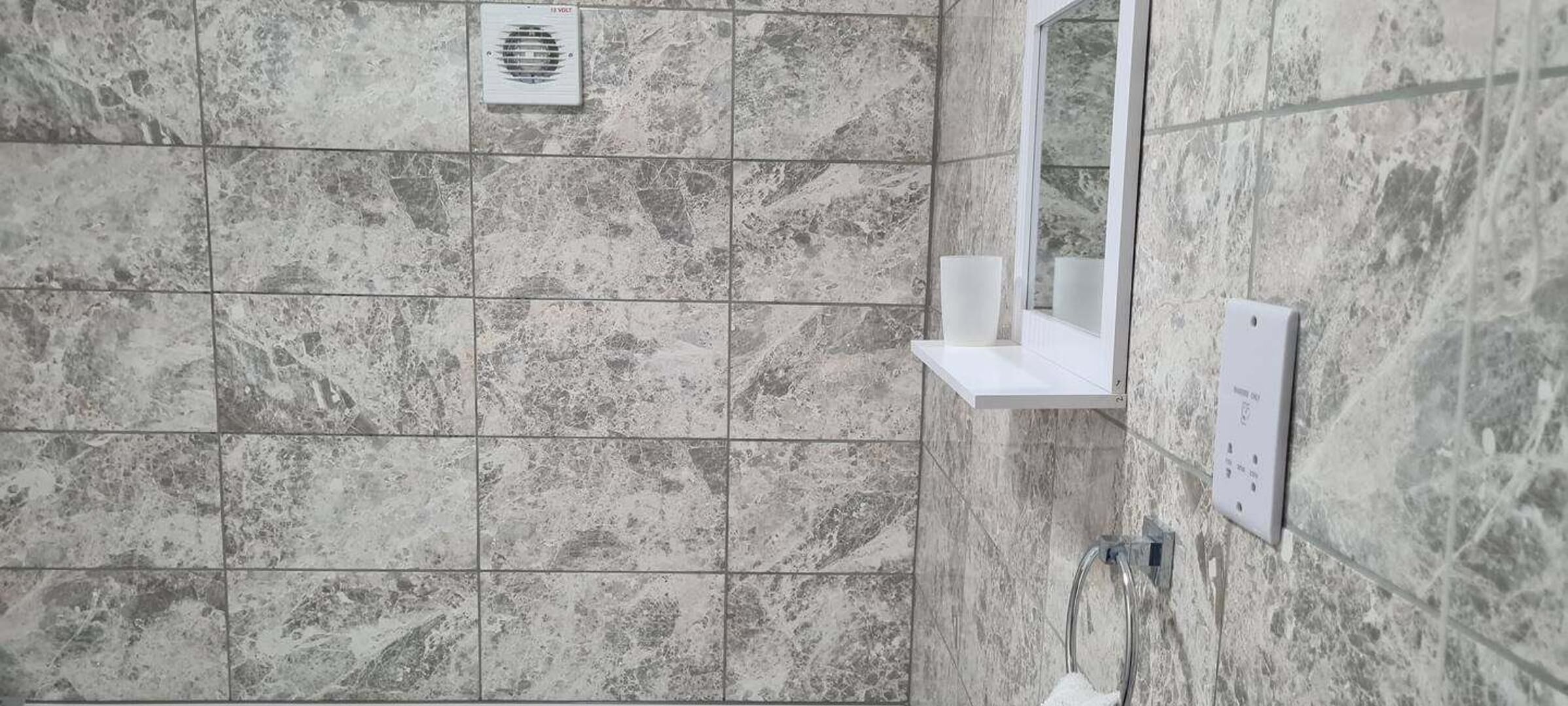 Un baño con baldosas de mármol, un cabezal de ducha, un espejo y un perchero para toallas.