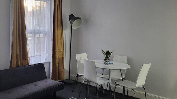 Una habitación moderna con un sofá gris, una mesita redonda con dos sillas y una lámpara de pie.