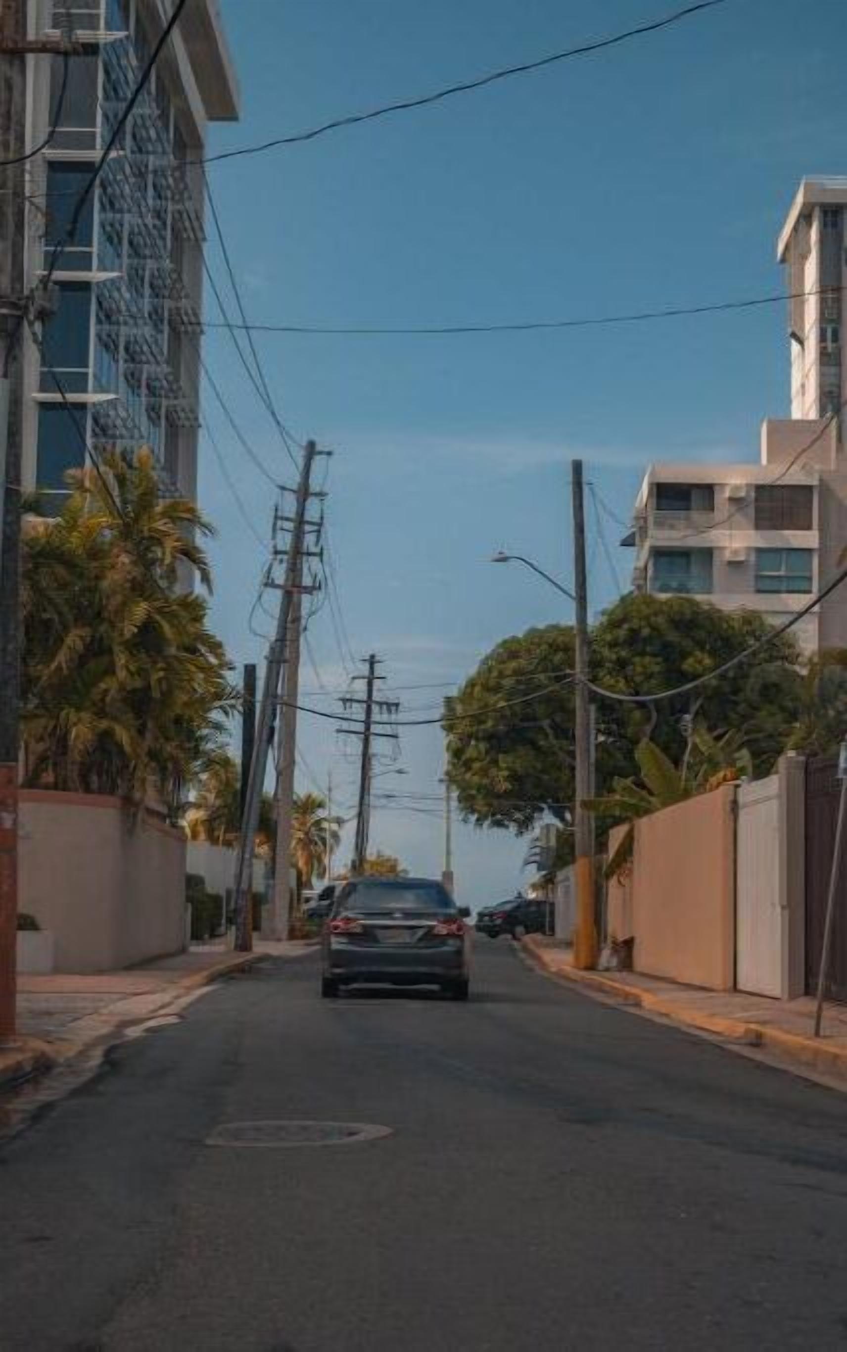 Une rue bordée de bâtiments des deux côtés, avec des lignes électriques aériennes et une voiture au loin.