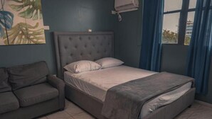 A bedroom with a bed, a couch, a wall-mounted air conditioner, and a window with curtains. - Sofia’s Beach Apartment (Carolina)