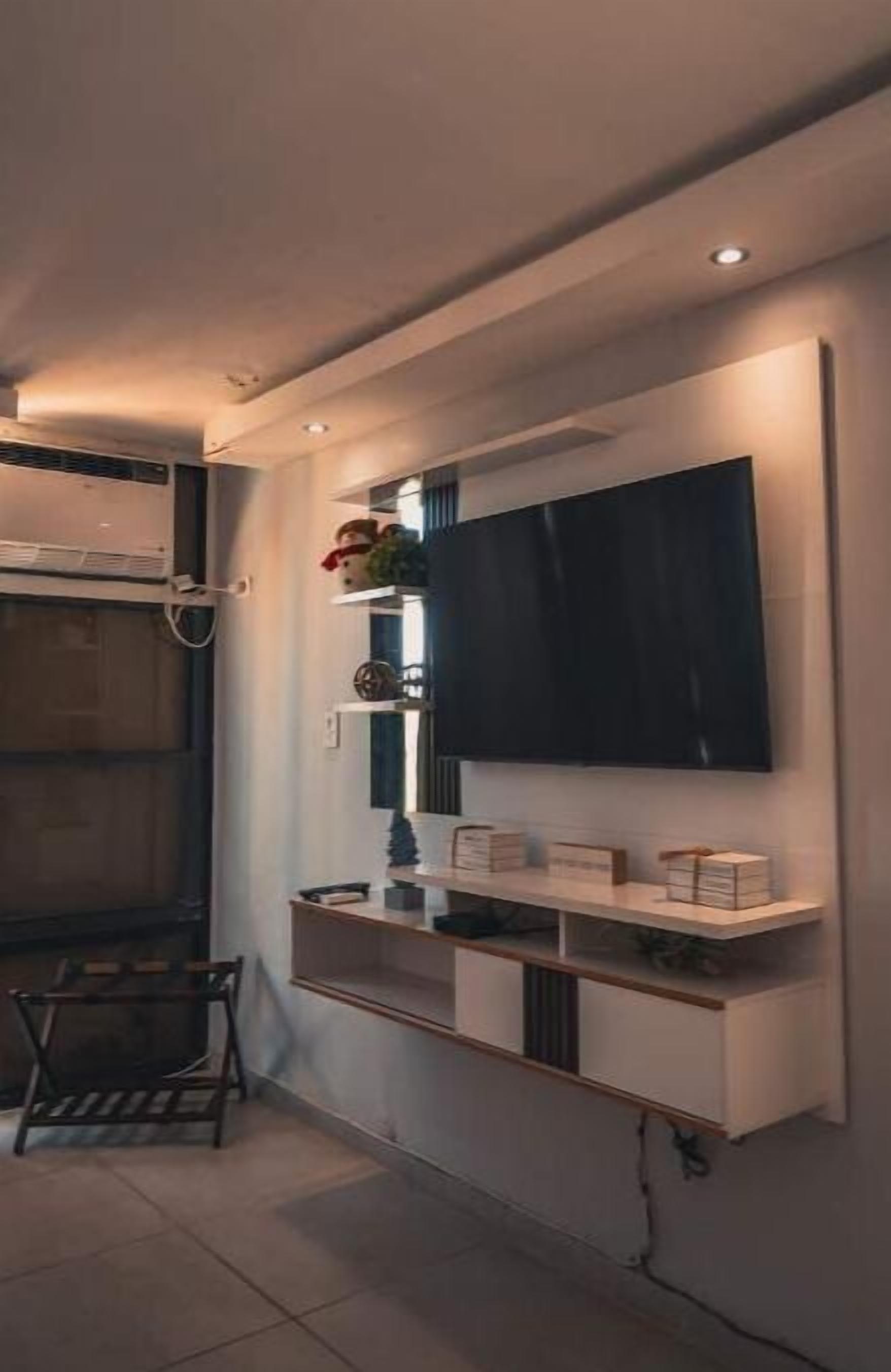 A modern kitchen with a built-in TV, wooden shelves, and a dining area with a bench.