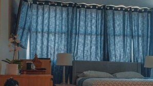 Une chambre à coucher comprenant un lit, des tables de chevet, des lampes, une commode et une fenêtre avec des rideaux.