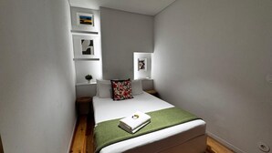 A small, modern bedroom with a single bed, a green throw blanket, and a small bedside table with a plant.