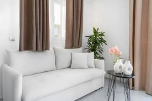 Uma sala de estar moderna com um sofá branco, cortinas marrons, uma planta em vaso e dois vasos brancos sobre uma mesinha.