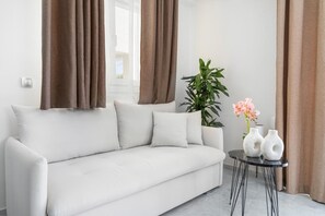 Un canapé blanc, une plante en pot et deux vases blancs sont posés sur une petite table ronde dans une pièce dont les rideaux sont marron.