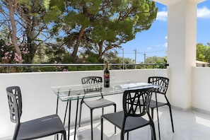 A glass-top table with four chairs, a bottle of wine, and two wine glasses on an outdoor balcony with a view of trees and a clear sky. - Apartment 'Miralis' with Mountain View, Wi-Fi and Air Conditioning (Nikiana)
