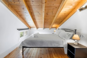 A bedroom with a wooden ceiling, a bed with white linens, a nightstand with a lamp, and a window. - Apartment 'Miralis' with Mountain View, Wi-Fi and Air Conditioning (Nikiana)