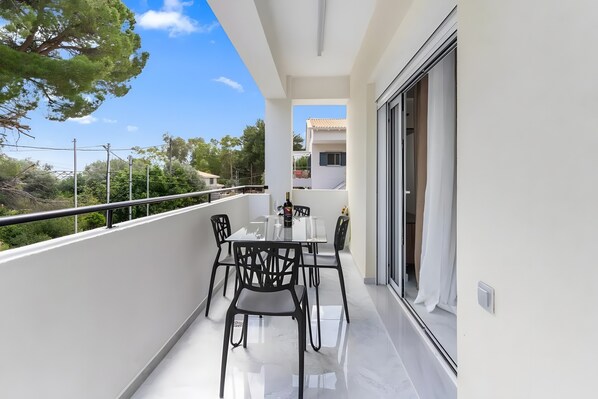 A balcony with a dining table and chairs, a sliding glass door, and a view of the surrounding area.