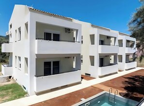 Un edificio moderno de varios pisos con balcones, piscina y cielo despejado.