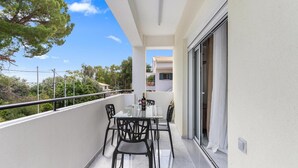 Un balcón con una mesa y sillas, una puerta de cristal y vistas del entorno.
