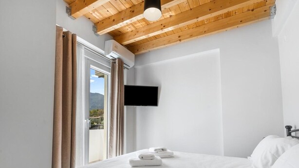 Un dormitorio con cama, televisor montado en la pared y ventana con cortinas.