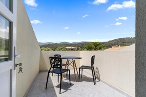 Un balcón con mesa y sillas, una puerta con llaves y vistas a colinas y edificios.