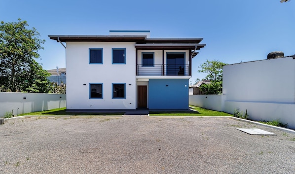 Une maison moderne à deux étages, dotée d’un toit plat, d’un balcon à l’étage supérieur et d’une allée gravillonnée.