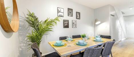 A dining area with a wooden table, grey woven chairs, and a potted plant.