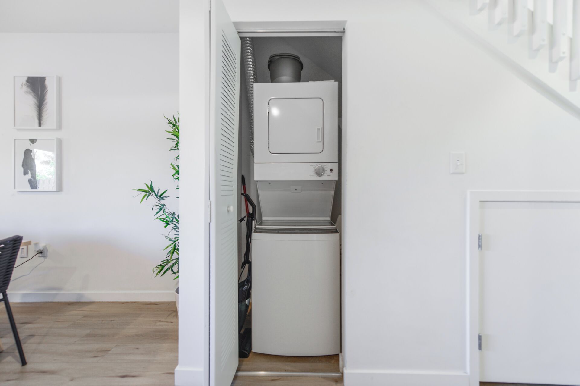 A compact laundry room with a washing machine and dryer, a potted plant, and a chair.