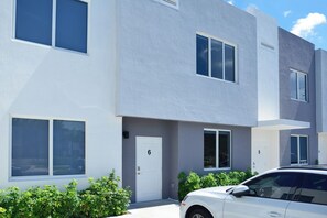Un edificio residenziale moderno a più piani, con porte numerate, ampie finestre e un'auto bianca parcheggiata nel vialetto.