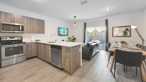 Une cuisine moderne dotée d’appareils électroménagers intégrés, d’un îlot central et d’un coin repas avec une table dressée pour quatre personnes.