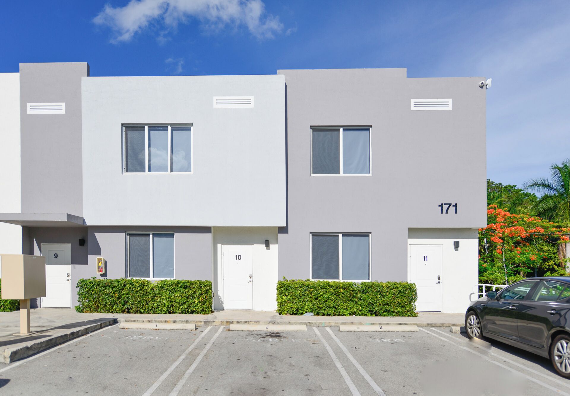 A modern two-story building with numbered doors 9 to 11, a parking area, and a car parked in front.