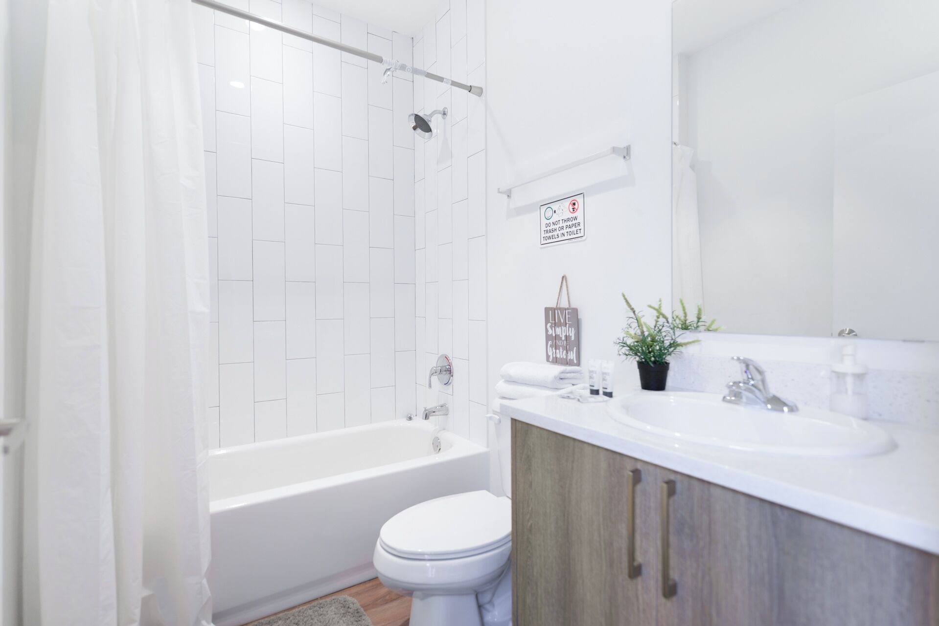 Un baño moderno con bañera, inodoro y lavamanos. Hay un cartel en la pared que indica no arrojar basura ni toallas de papel en el inodoro.