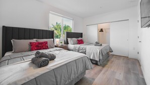 Une chambre moderne avec deux lits, une fenêtre donnant sur des palmiers et un plancher en bois.