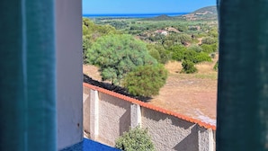 A view from a window overlooking a rural landscape with a clear blue sky, a distant coastline, and scattered buildings. - Ostello Brebei Niedda (Gonnesa)