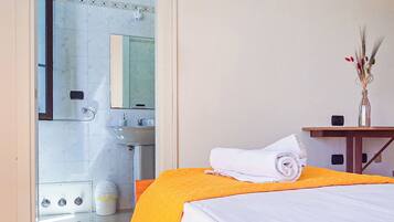 Ein Hotelzimmer mit Bett, einem durchgegangenen Tür erkennbaren Badezimmer und einem kleinen Tisch mit einer Vase.