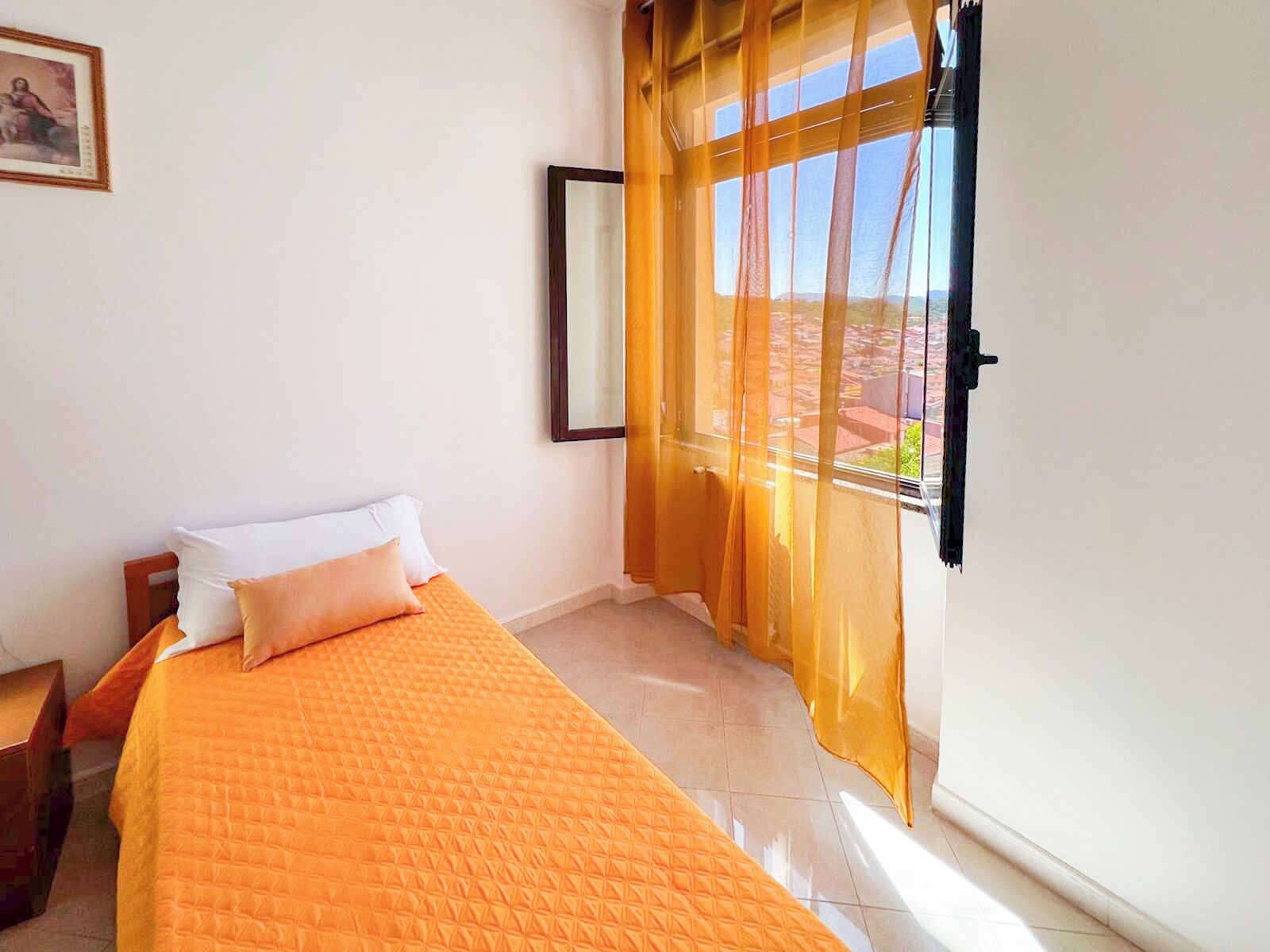 A bedroom with a bed, a nightstand, a window with curtains, and a framed picture on the wall.