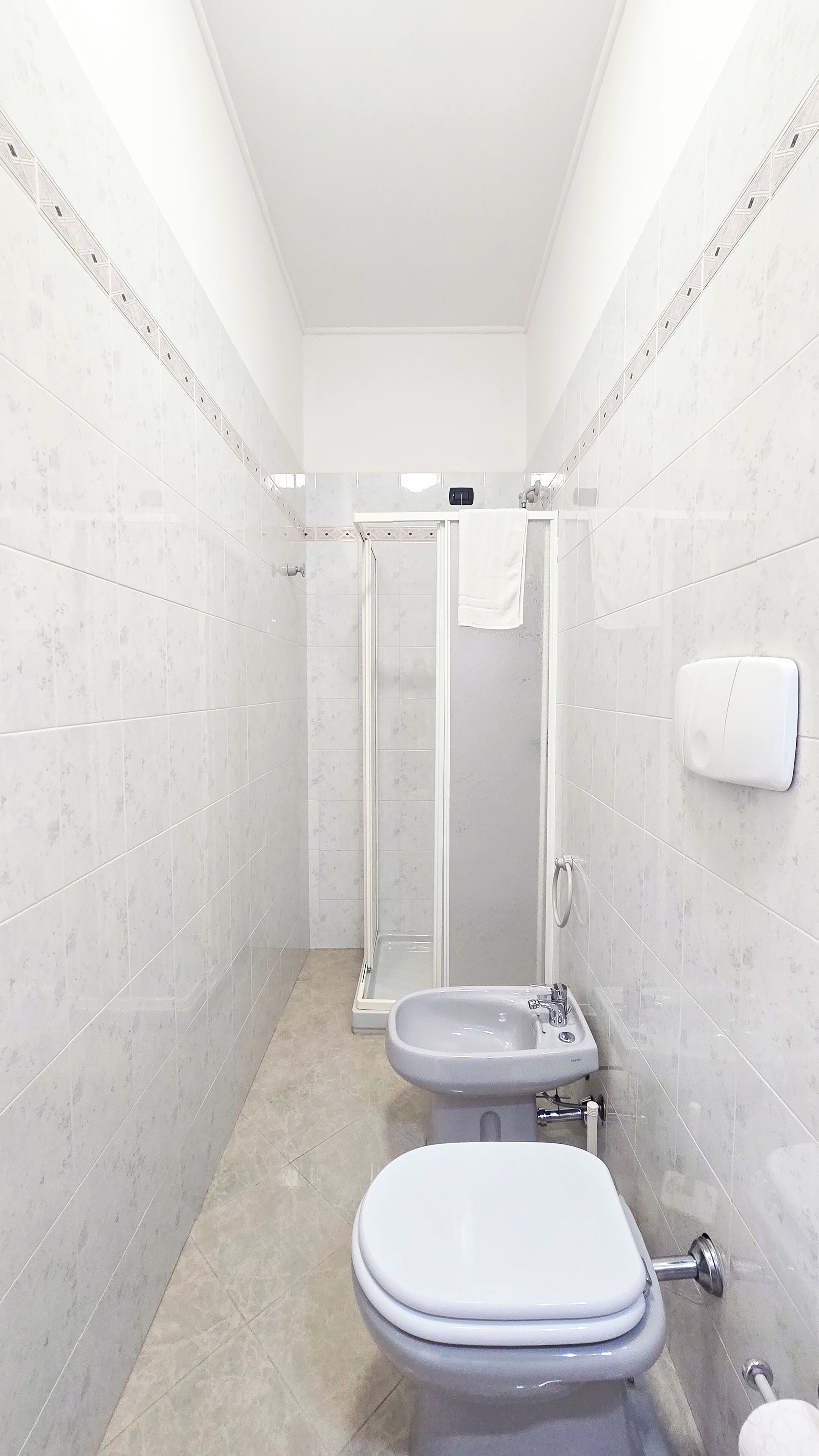 Une petite salle de bain comprenant des toilettes, un lavabo et une douche fermée par une paroi de verre.
