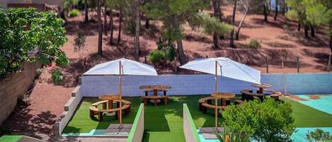 A patio area with outdoor seating and umbrellas, surrounded by trees and a pool.