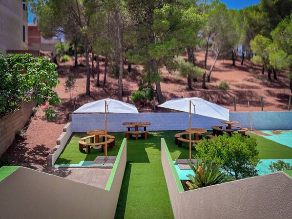 Un patio con mobiliario exterior y sombrillas, rodeado de árboles y una piscina.