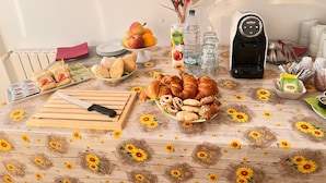 A breakfast table with pastries, fruits, and a coffee maker. - Ostello Brebei Niedda (Gonnesa)