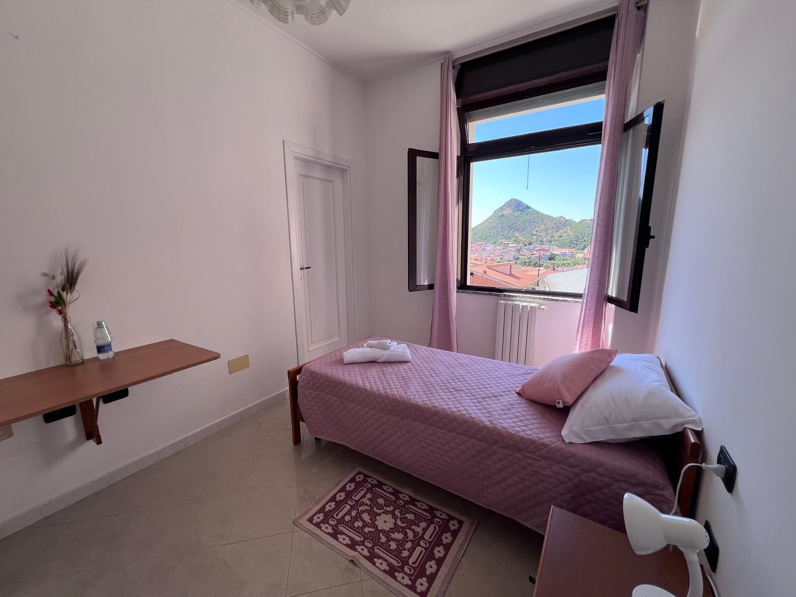 Un dormitorio con cama, mesita de noche, ventana y vistas a la montaña, además de un radiador.