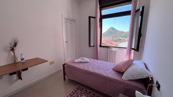 Un dormitorio con cama, mesita de noche, ventana y vistas a la montaña, además de un radiador.