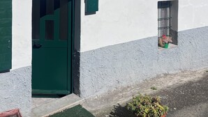 Ein weißes Gebäude mit grünen Fensterläden, einer grünen Tür und einem kleinen Fenster mit einer Pflanze.