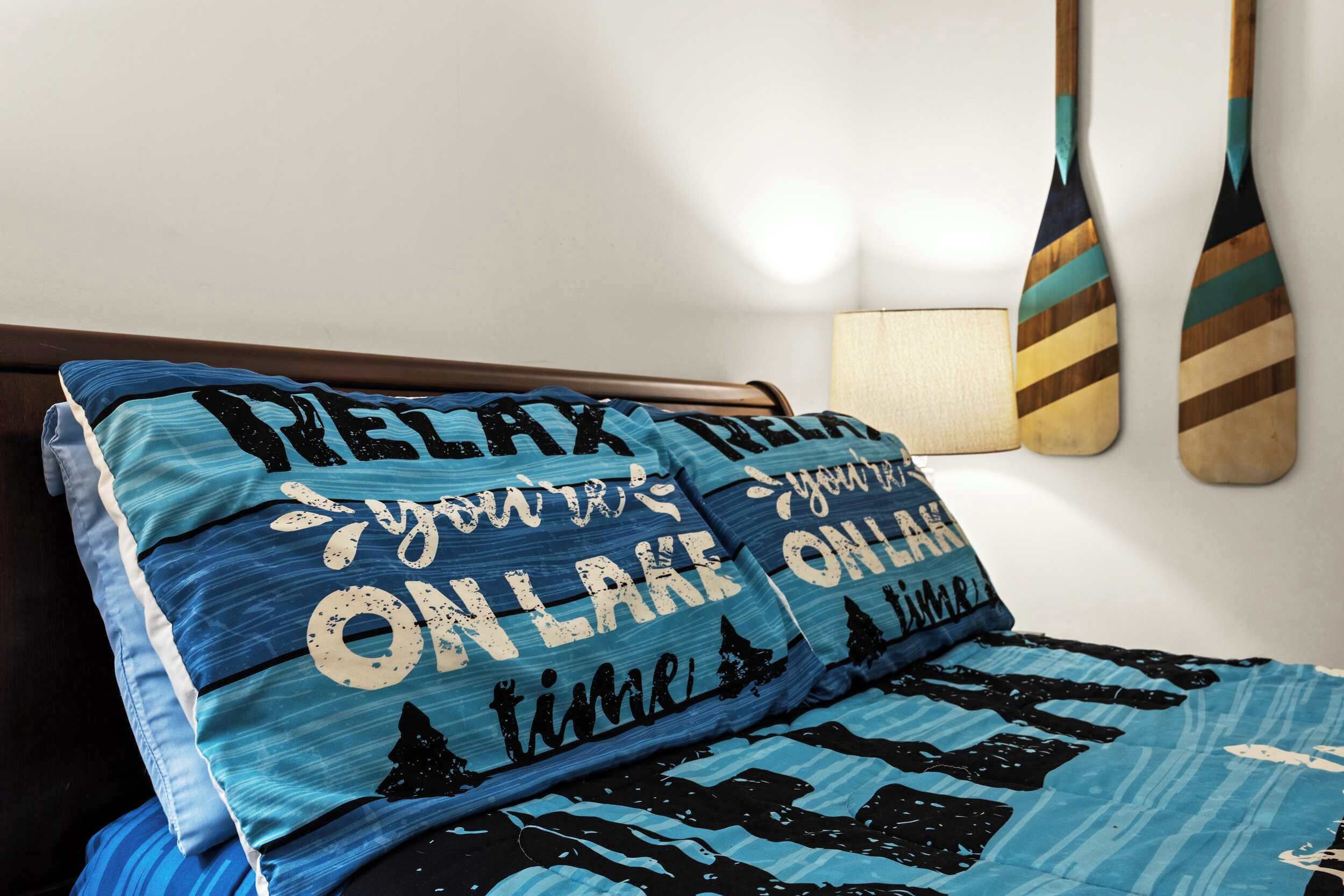 Ein Bett mit blau-schwarzem Muster auf der Bettwäsche, zwei Holzschläger an der Wand und eine kleine Wandlampe.