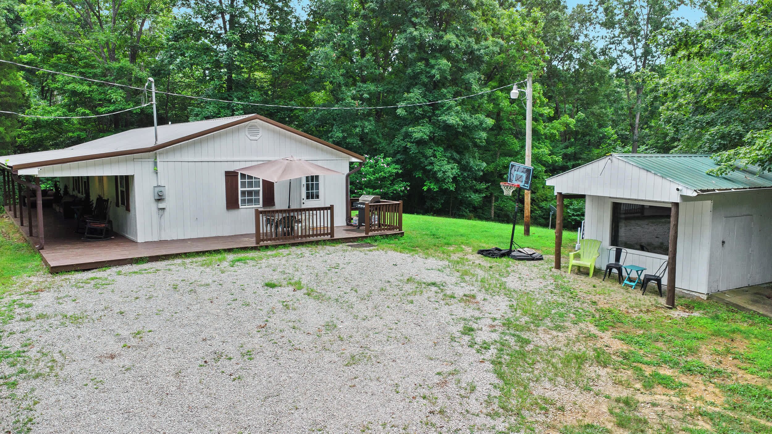 A small, single-story house with a porch, a basketball hoop, and a shed.