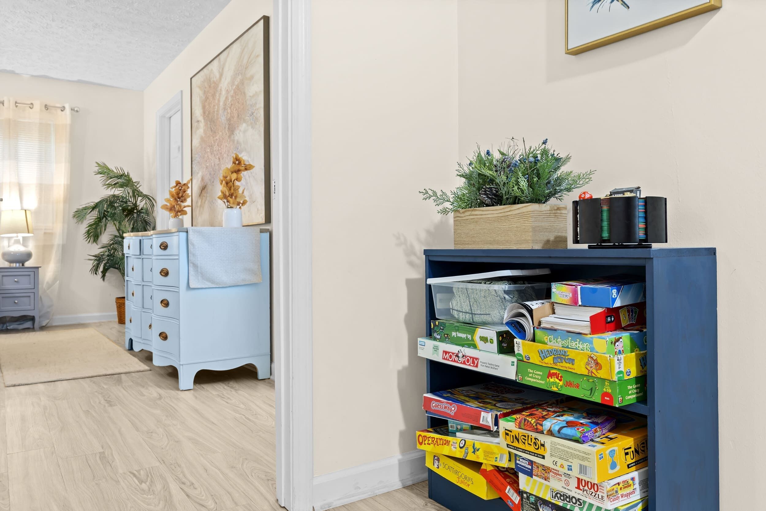 Een kamer met een blauwe boekenkast vol gezelschapsspellen, een lichtblauwe dressoir en een schilderij aan de muur.