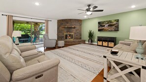 Una sala de estar con chimenea de piedra, ventilador de techo y vistas al exterior.